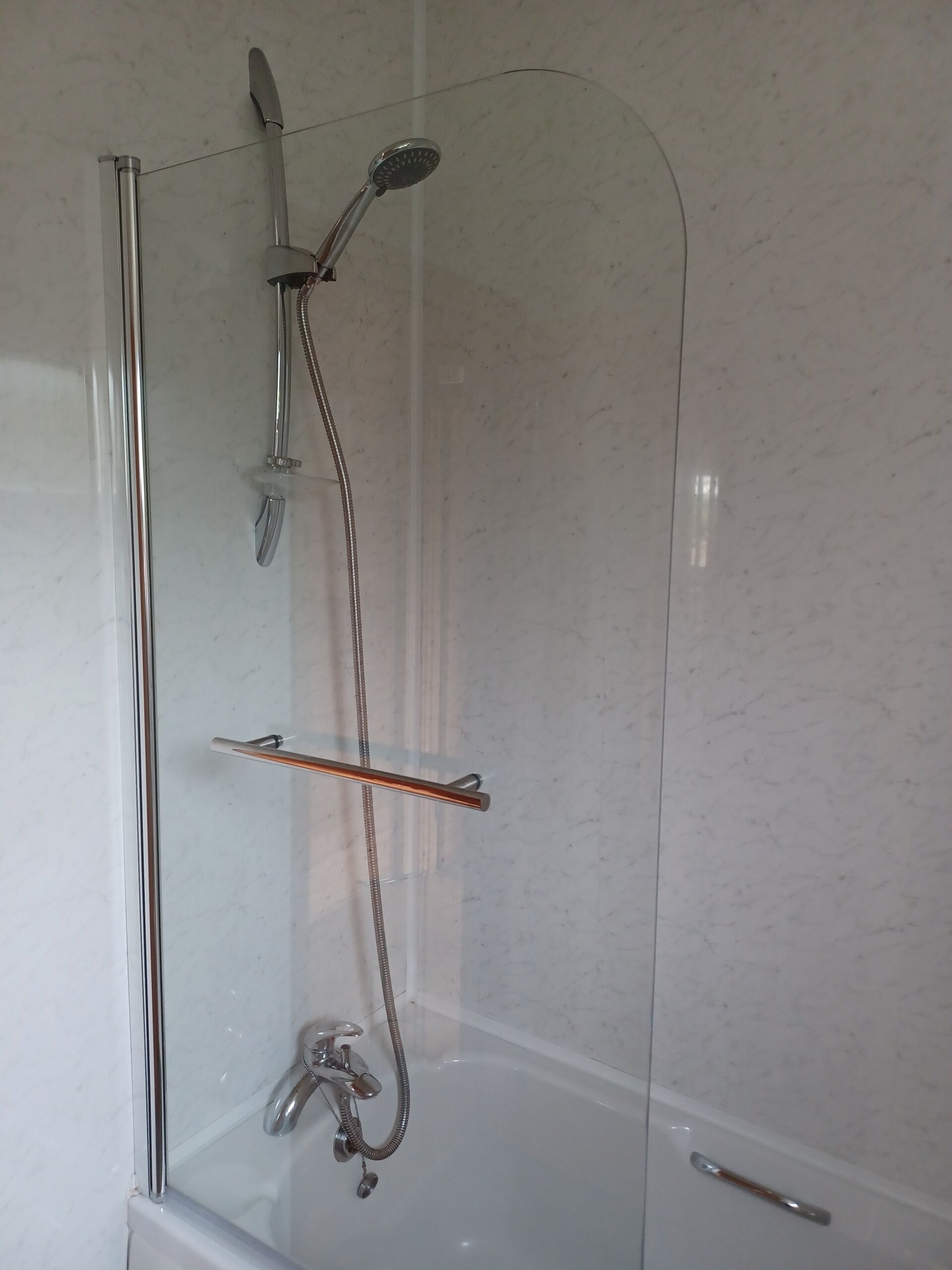 A glass-enclosed shower with a handheld showerhead, a fixed showerhead, and a handheld faucet.