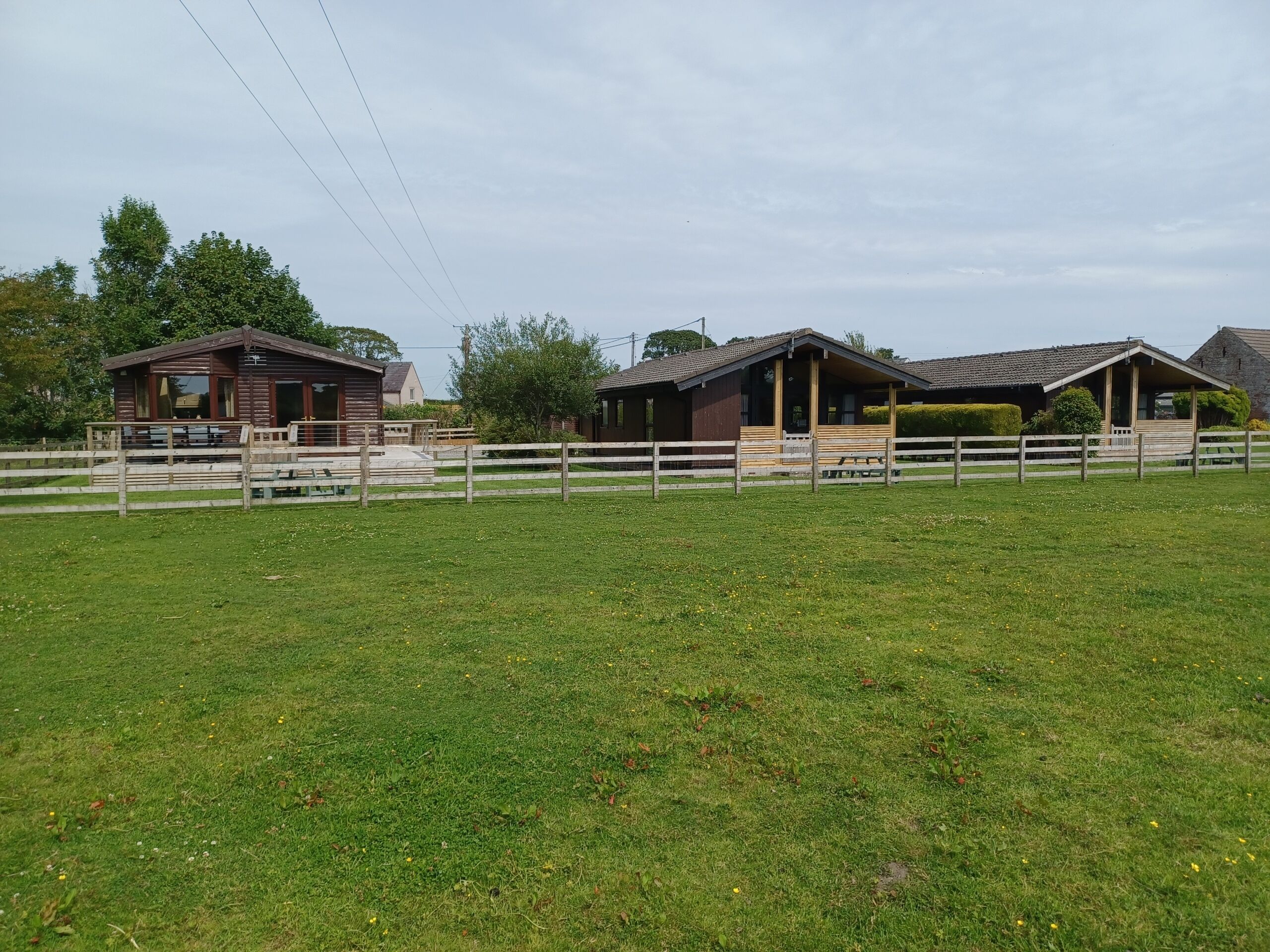 A fenced pasture with three wooden buildings, each with a porch and a covered area.