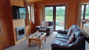 L’intérieur chaleureux d’un chalet avec une cheminée, des canapés en cuir, une table basse en bois et un téléviseur fixé au mur.