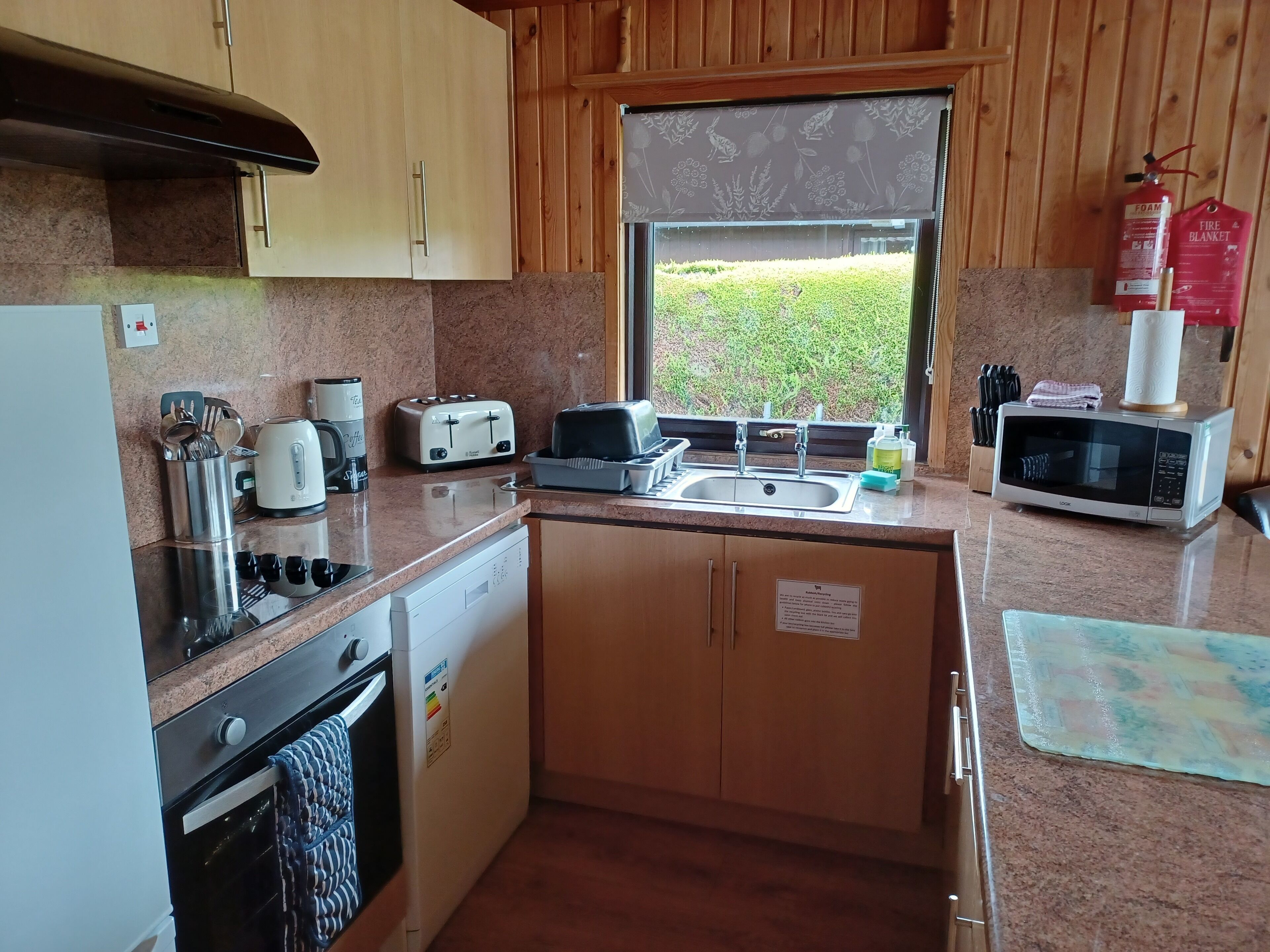 Een kleine keuken met houten kastjes, een RVS spoelbak, een broodrooster, een magnetron en een vaatwasser.