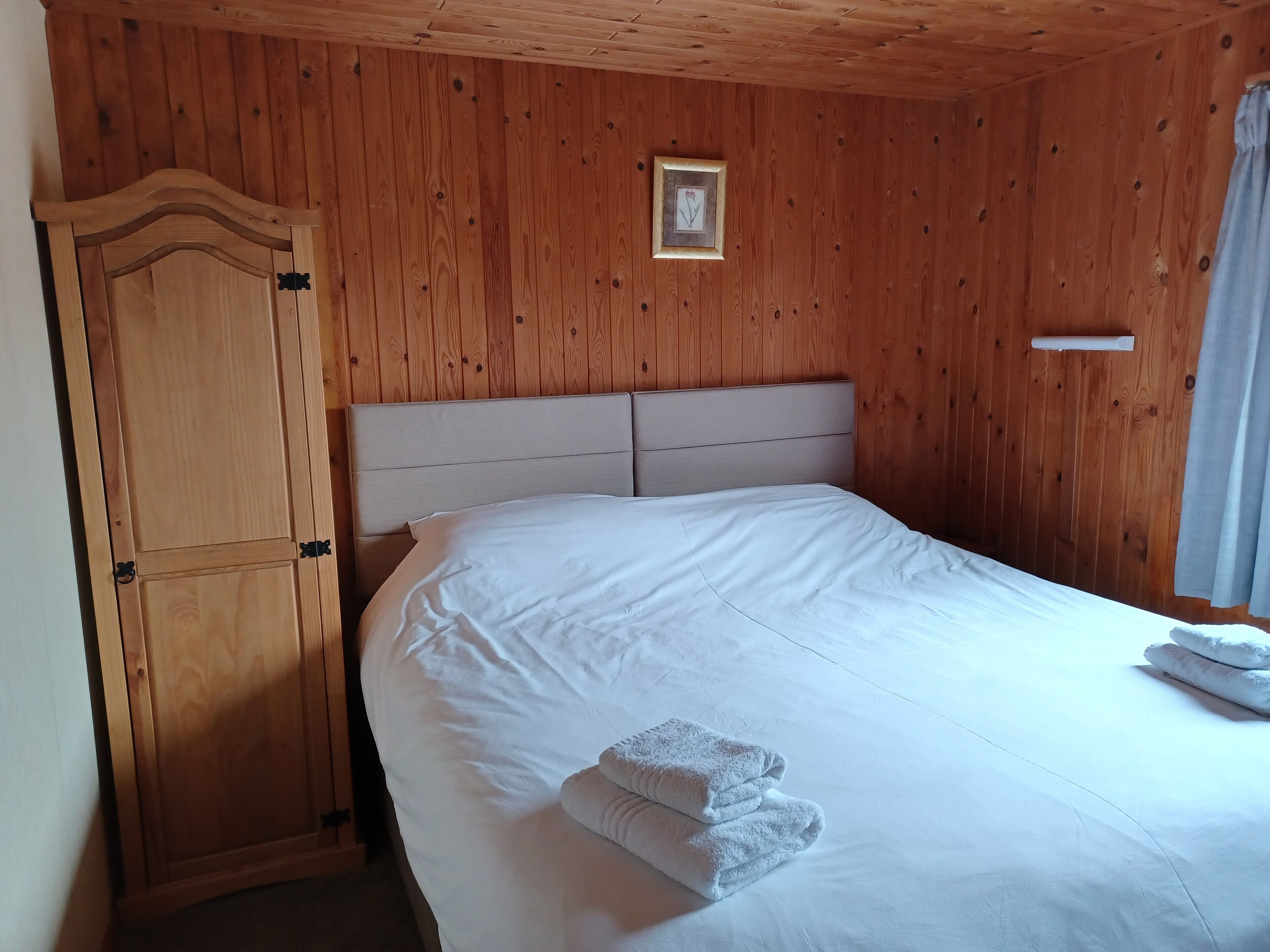 Une pièce aux murs lambrissés, avec un lit, une armoire et un tableau encadré.