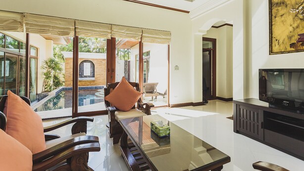 A spacious living area with a large glass wall, a pool, and a television.