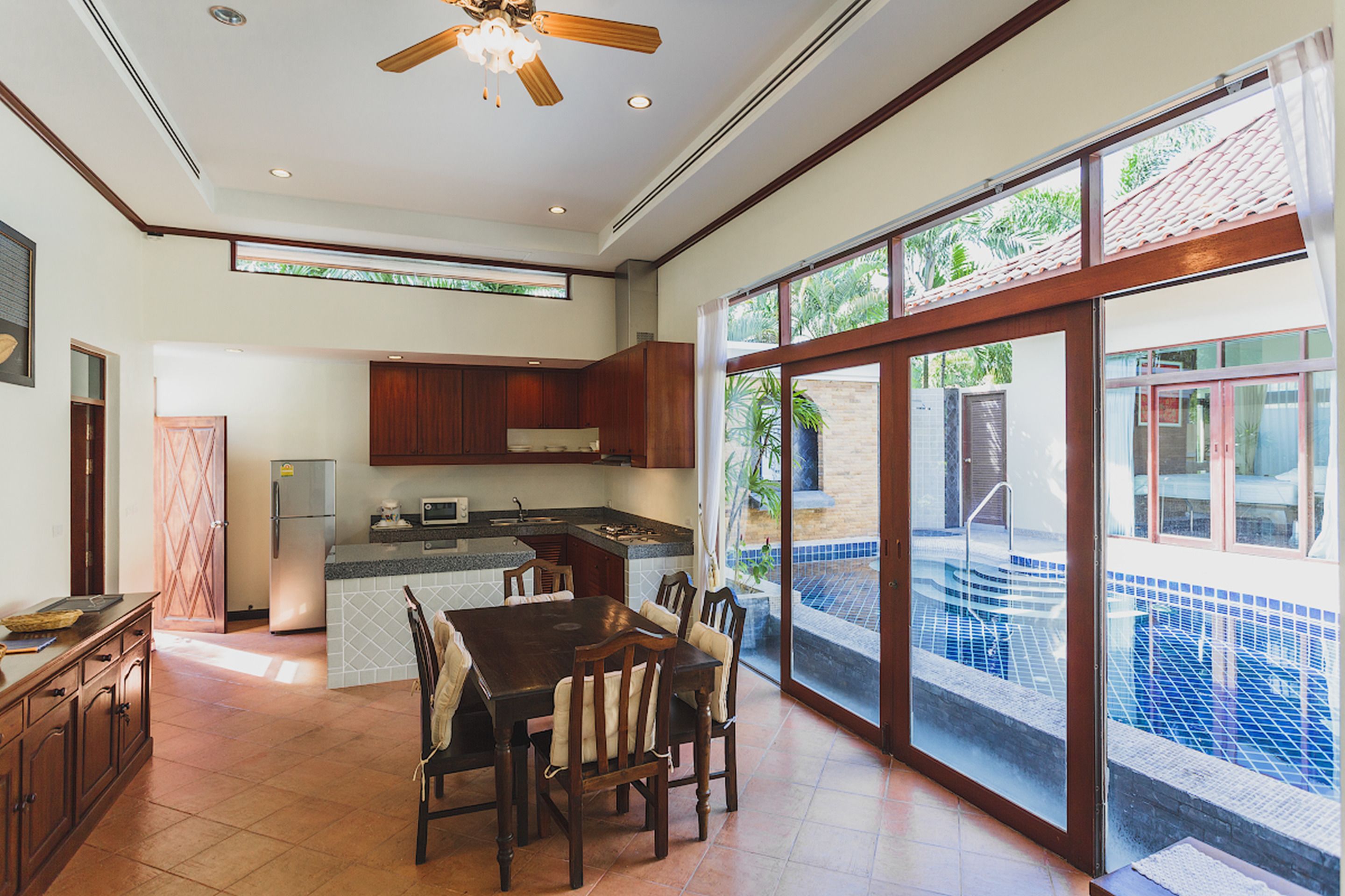 A spacious kitchen with a large island, a dining area with a wooden table and chairs, and a view of a swimming pool through large sliding glass doors.