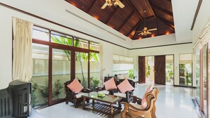 A spacious living area with a wooden ceiling, large windows, and a television on a stand.