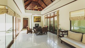 A spacious living area with a high ceiling, a television, a dining table with chairs, and a sofa.