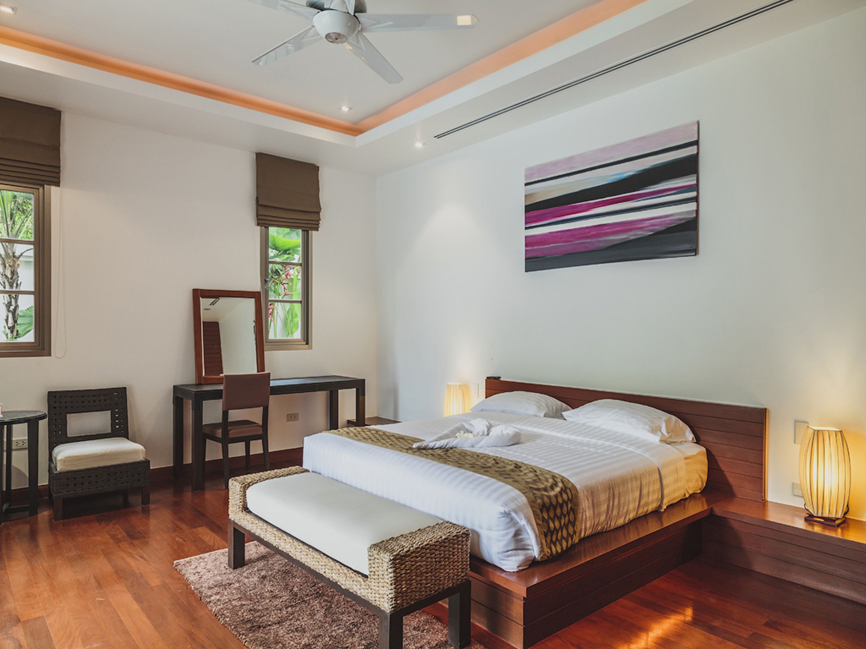 Une chambre à coucher avec un grand lit, un bureau, une chaise, un banc et un ventilateur de plafond.