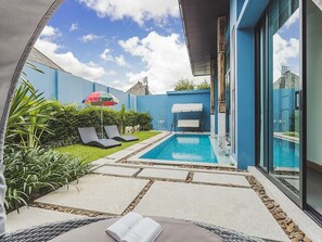 Un espace piscine extérieur moderne, doté de chaises longues, d’un petit bassin et d’une véranda fermée par des baies vitrées.