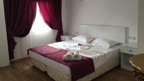 A neatly made bed with white linens and a pink blanket, a bedside table with a lamp, and a window with red curtains. - Cohiba Hotel (Bodrum)