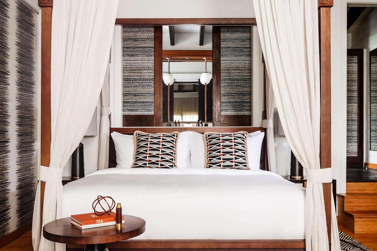 A four-poster bed with white drapes, a patterned rug, and a bedside table with a book.