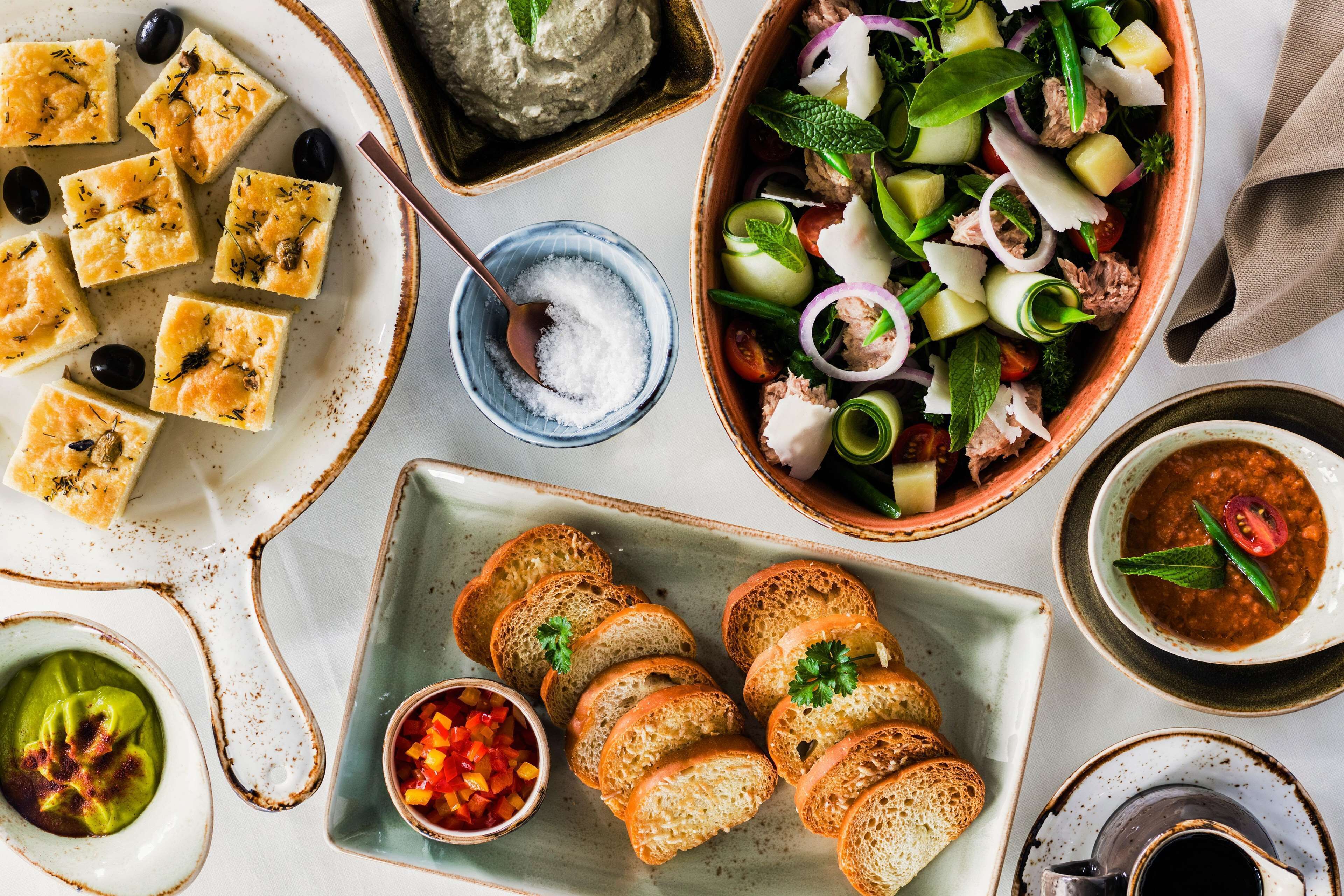 Diversos alimentos, entre ellos pan, aceitunas y una ensalada con queso y verduras.
