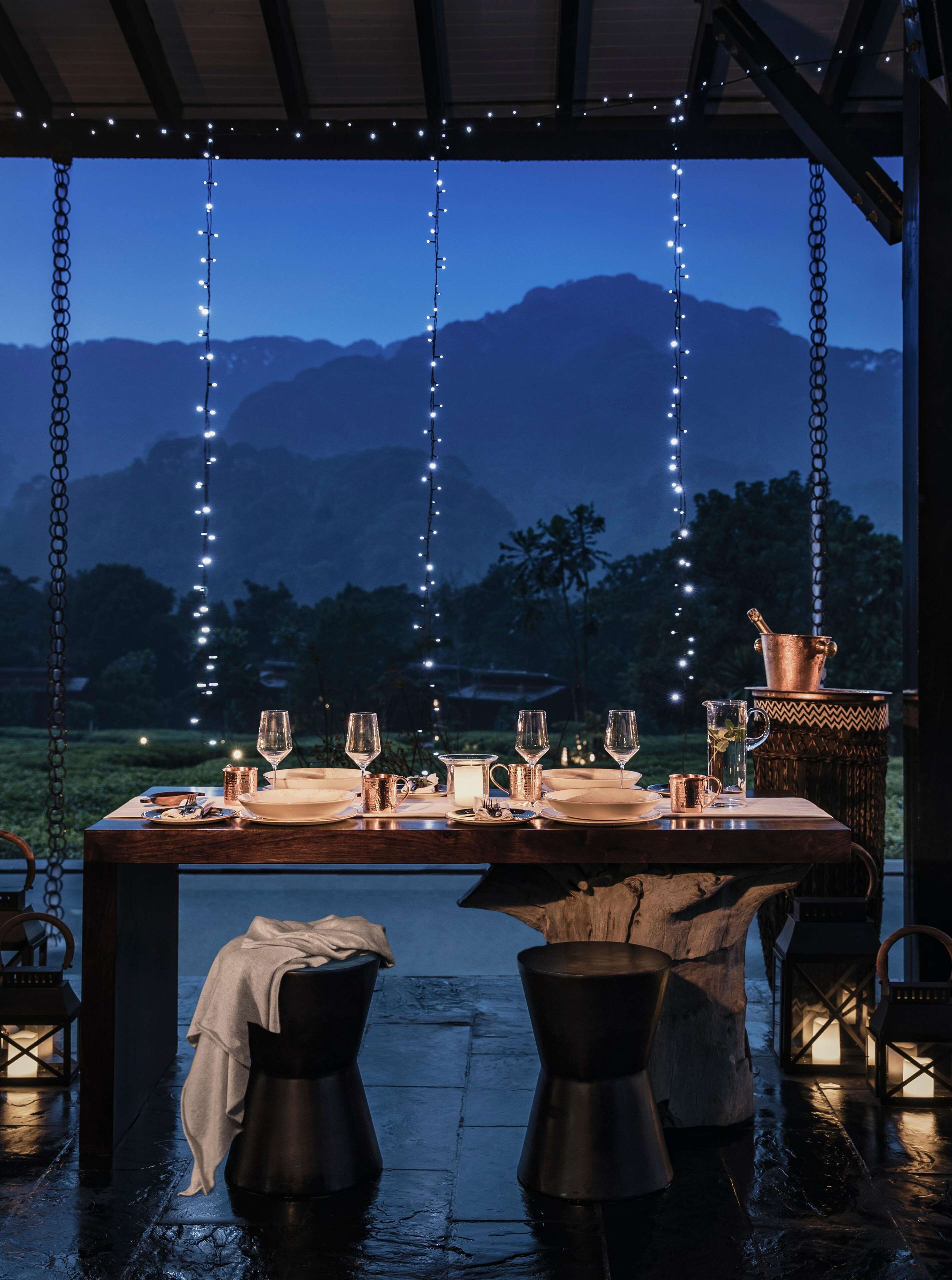A dining table set for four with a view of mountains, string lights, and a rustic setting.