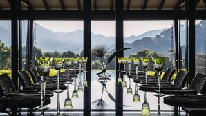 A dining area with a table set for six, surrounded by chairs, with a view of mountains in the background. - One&Only Nyungwe House (Bushekeri)