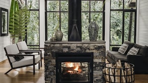 A cozy living room with a fireplace, wooden beams, and large windows. - One&Only Nyungwe House (Bushekeri)