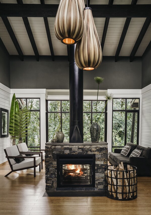 A cozy living room with a fireplace, wooden beams, and large windows. - One&Only Nyungwe House (Bushekeri)