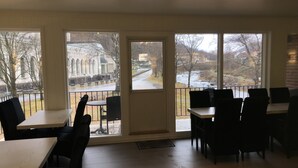 A dining area with large windows, wooden flooring, and black chairs. - Rjukan Gjestehus (Tinn)