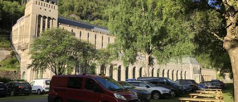 Un estacionamiento con automóviles y mesas de picnic frente a un edificio con una torre y ventanas arqueadas.