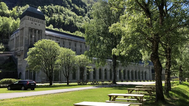 A building with a stone facade and arched windows, surrounded by a grassy area with picnic tables. - Rjukan Gjestehus (Tinn)