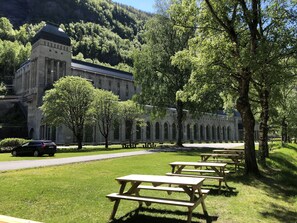 A building with a stone facade and arched windows, surrounded by a grassy area with picnic tables. - Rjukan Gjestehus (Tinn)