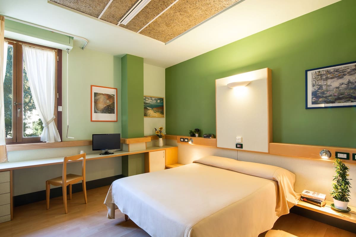 A hotel room with a bed, desk, chair, and a window with curtains.