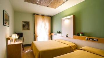 A hotel room with two beds, a desk with a lamp, a television, and a window with curtains.