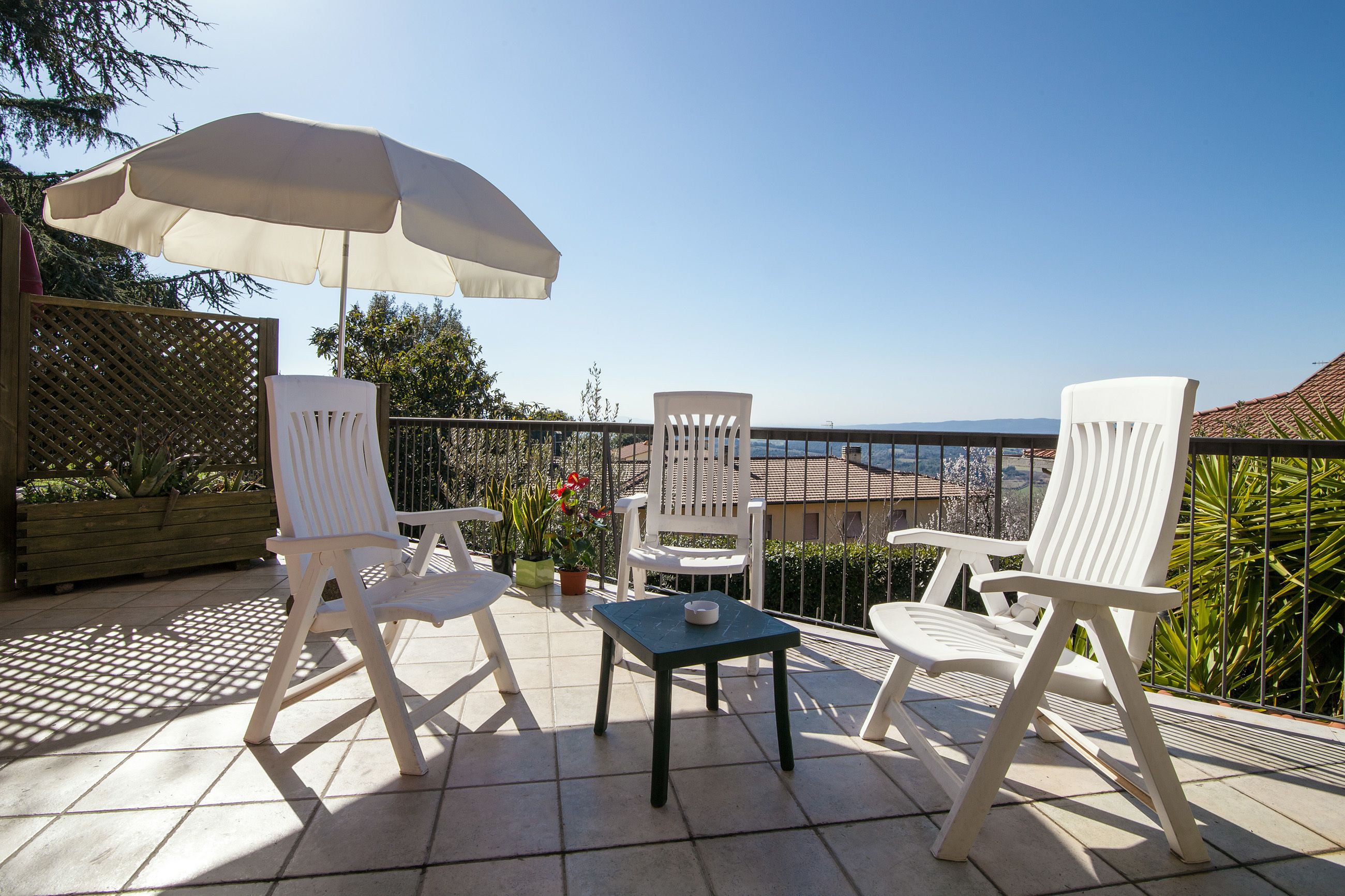 A patio with two white chairs, a table, and a large umbrella.