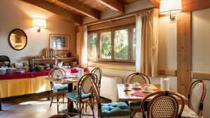 A cozy dining area with wooden furniture, a buffet table with food items, and a window with curtains. - Hotel Duca Del Mare (Massa Marittima)
