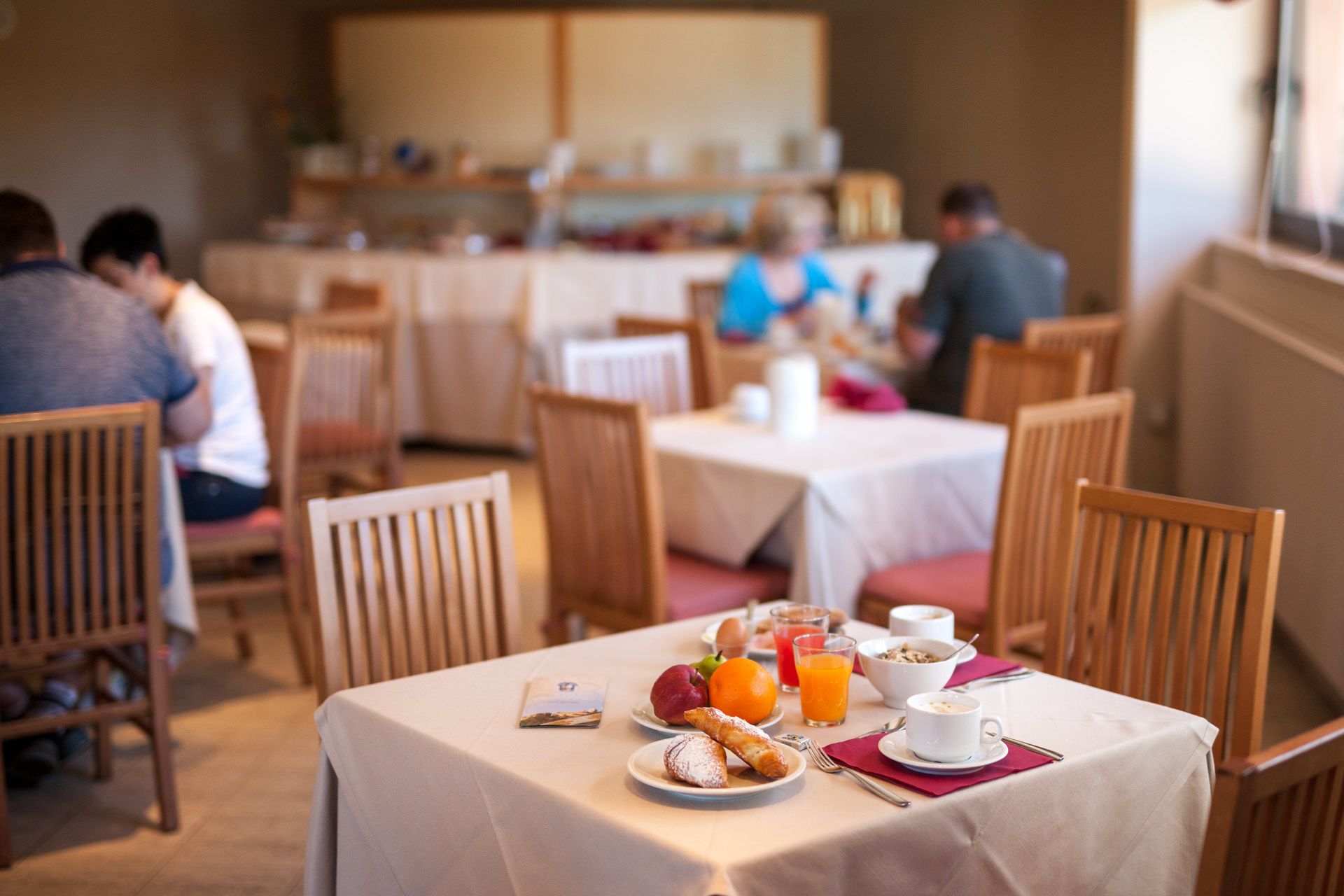 A breakfast setting with tables, chairs, and breakfast items like pastries, fruit, and beverages.