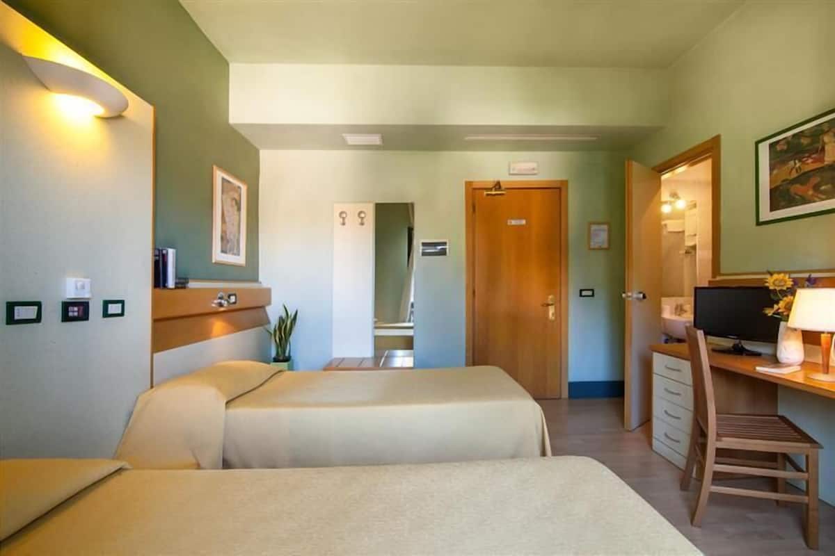 A hotel room with two beds, a desk with a computer, a chair, and a TV.