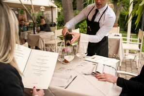 A waiter pouring wine into a glass at an outdoor restaurant. - Hotel Duca Del Mare (Massa Marittima)