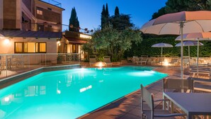 A swimming pool with lounge chairs and umbrellas, surrounded by a building with a balcony and a view of trees. - Hotel Duca Del Mare (Massa Marittima)