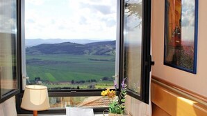 A room with a large window offering a view of green fields and distant hills. - Hotel Duca Del Mare (Massa Marittima)