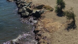 A beach with rocky shoreline, clear blue water, and distant mountains.