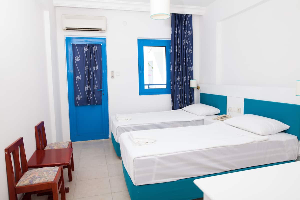 A hotel room with two beds, a blue door, a mirror, and a small table with chairs.