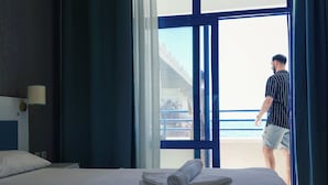 A hotel room with a bed, a rolled towel, a nightstand, and a window with curtains.