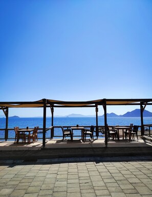 A covered outdoor seating area with tables and chairs, overlooking a body of water and distant mountains. - One More Day Hotel (Bodrum)