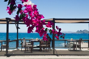 Un patio frente al mar con mesas y sillas, con vista al océano.
