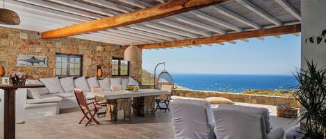 A covered outdoor seating area with stone walls, a white sofa, and a table.