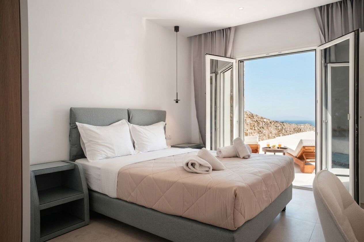 Ein modernes Schlafzimmer mit Bett, Nachttischen, Meerblick und einem Balkon.