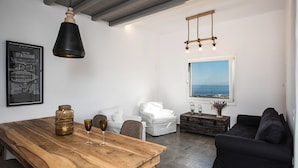 Een moderne woonkamer met een houten eettafel, witte banken en een groot raam met uitzicht op zee.