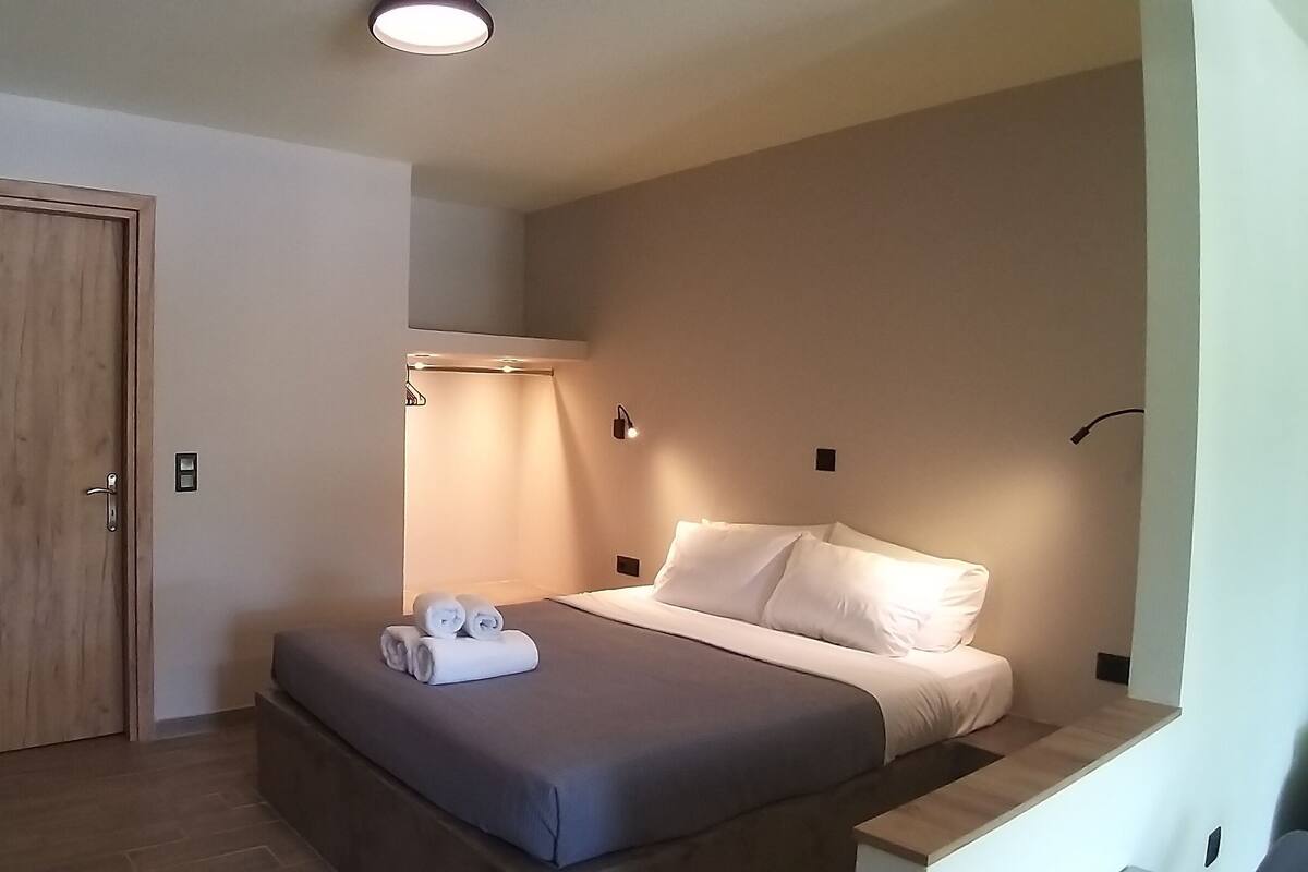 A bedroom with a bed, a wooden door, a small wooden bench, and a wall-mounted light.
