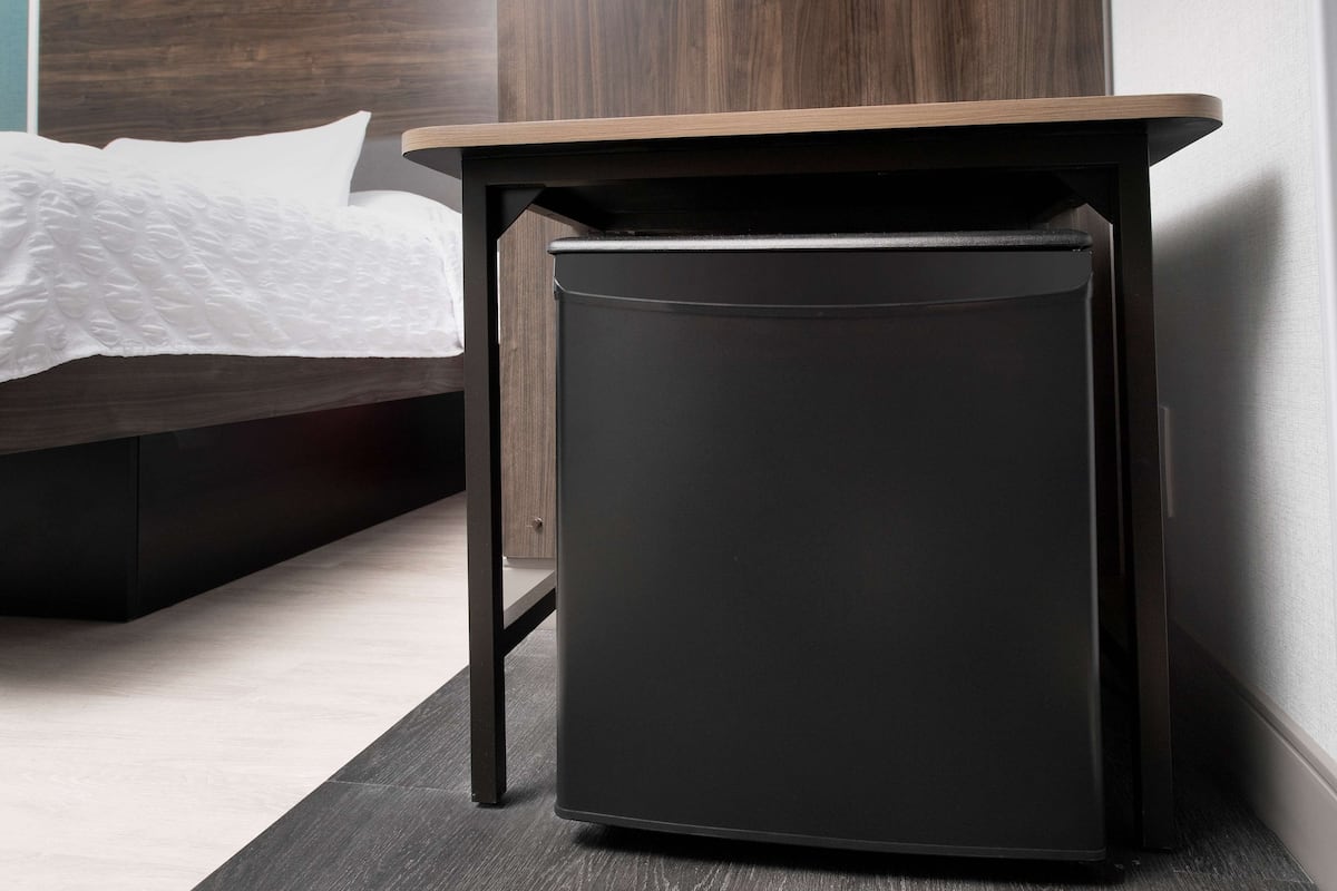 Une petite table d’appoint noire, dotée d’un plateau en bois, placée à côté d’un lit recouvert d’une couvre-lit blanche à motifs.
