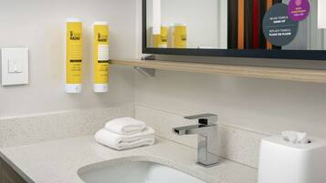 A modern bathroom with a sink, mirror, and toiletries. There are instructions for towel reuse and a tissue box.