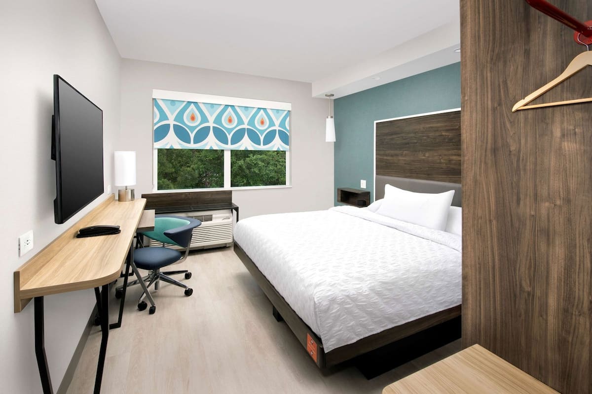 Une chambre d’hôtel équipée d’un lit, d’un bureau, d’une chaise, d’une télévision et de fenêtres donnant sur un paysage agréable.
