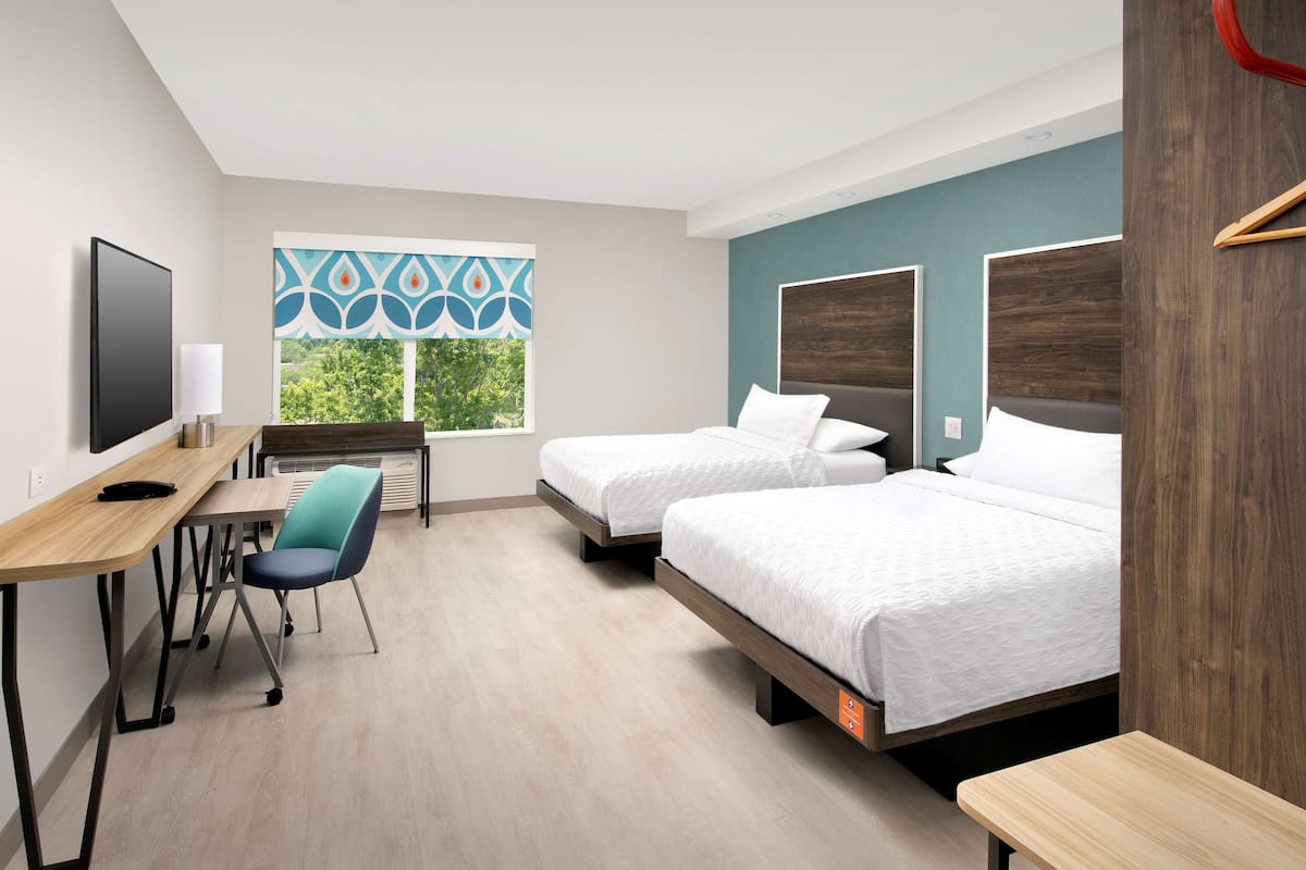 Une chambre d’hôtel avec deux lits, un bureau, une chaise et un téléviseur.