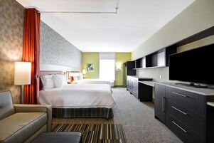 Una habitación de hotel con dos camas, un sofá, un televisor y una kitchenette.