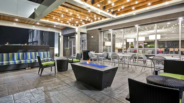 Un espace extérieur aménagé en terrasse, avec un foyer, des sièges et une vue sur l’intérieur.