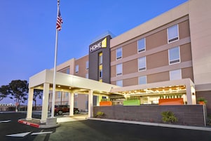Un hotel de varios pisos con un letrero que dice "HOME 2", un acceso cubierto y un área de estacionamiento.