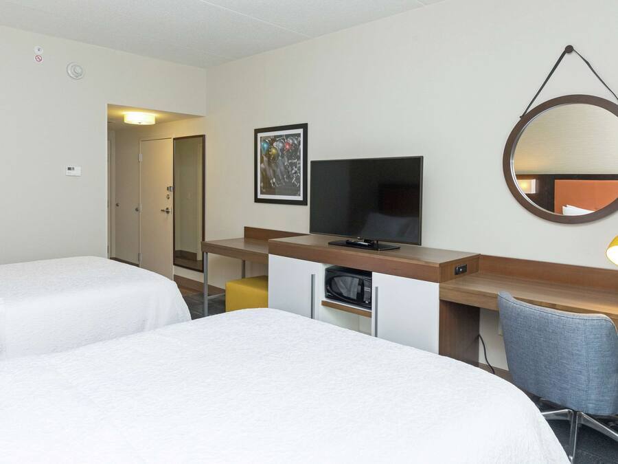 Quarto de hotel com duas camas, uma escrivaninha com computador, televisão, micro-ondas e um espelho.