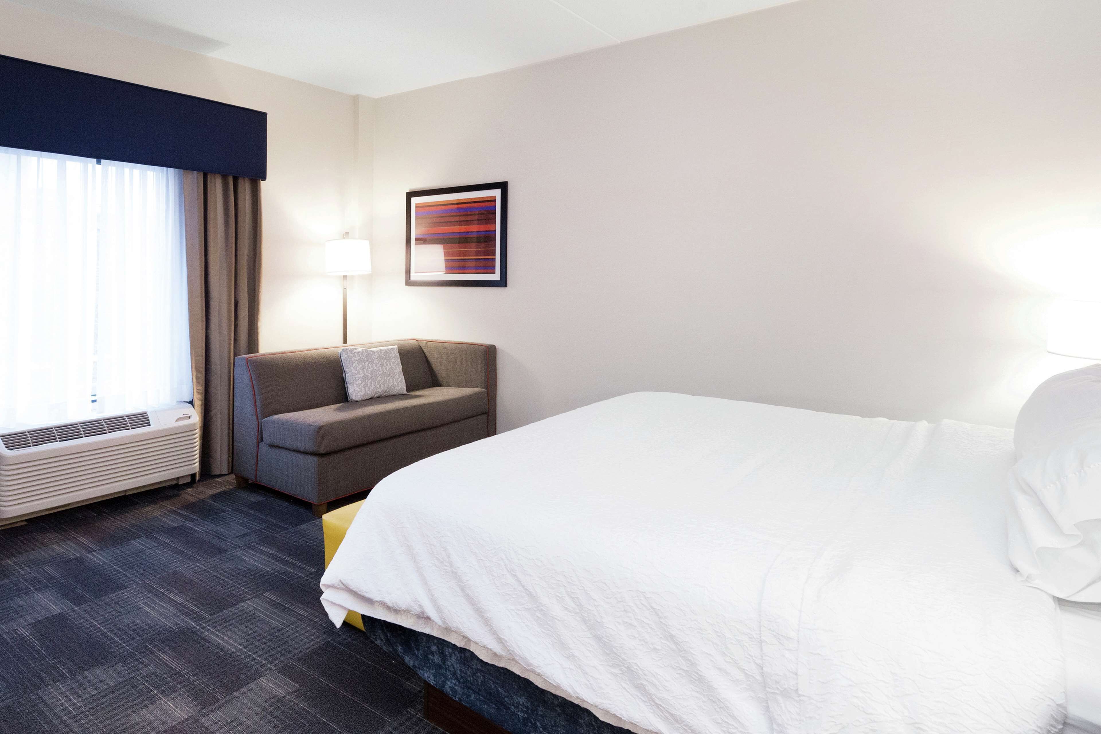 A hotel room with a large bed, a sofa, a desk, a lamp, and a window with curtains.