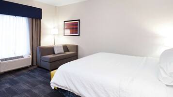 A hotel room with a large bed, a sofa, a desk, a lamp, and a window with curtains.